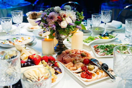 Luxurious banquet table set with cured meats, cheeses, fresh fruits, and a floral centerpiece under soft candlelight for an upscale event.の写真素材