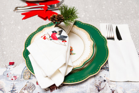Festive holiday table arrangement with decorative green plates, embroidered napkin featuring a...