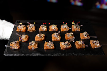 Elegant bite-sized canapÃ©s with golden bread, microgreens, and translucent caviar pearls served on a black slate tray.の写真素材