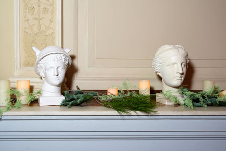 White Greco-Roman style busts displayed on a mantle with pine branches and candles for a festive...