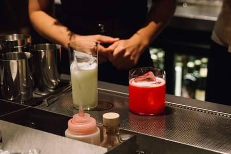 Two vibrant cocktails, one red and one green, served with ice at a bar counter, ready for guests during a nightlife scene.の写真素材