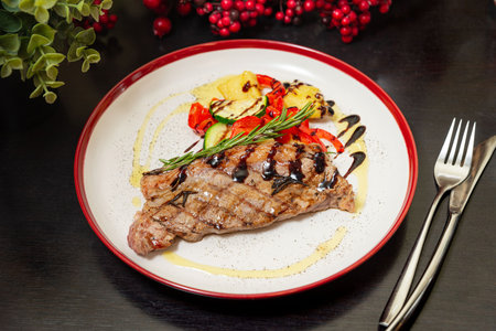 Juicy grilled beef steak with balsamic glaze served with roasted vegetables and rosemary on a white plate with red rim.の写真素材