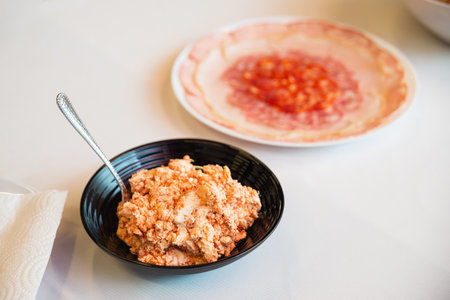 Close-up of a bowl of spicy ricotta cheese spread, served alongside a plate of assorted sliced cured meats on a table.の写真素材