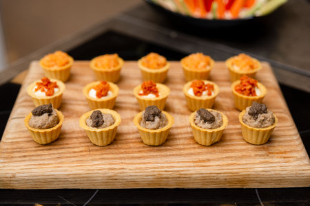 A variety of bite-sized savory tartlets arranged neatly on a wooden board, perfect for catering or party finger food ideas.の写真素材