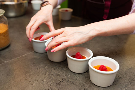 Close-up of hands arranging individual raspberry panna cotta desserts in white ramekins, perfect for elegant events and catering menus.の写真素材