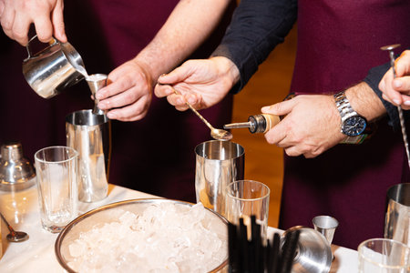 Close-up of bartenders mixing drinks using shakers, measuring spoons, and pouring ingredients during a cocktail-making session.の写真素材