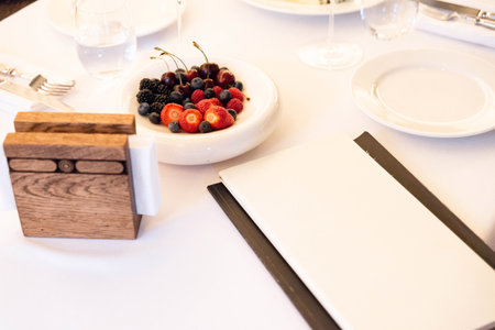 Close-up of a white plate with strawberries, cherries, blueberries, and blackberries on a neatly set restaurant table.の写真素材