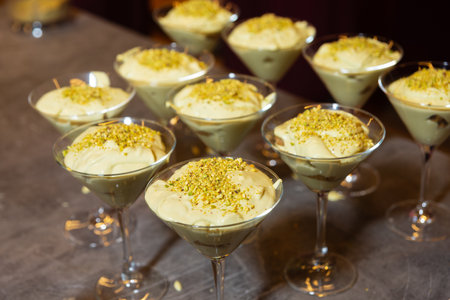 Several pistachio mousse desserts served in martini glasses, topped with crushed nuts, arranged on a counter for presentation.の写真素材