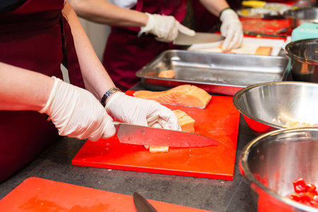 Close-up of participants slicing fresh salmon on red cutting boards in a professional kitchen or culinary workshop setting.の写真素材
