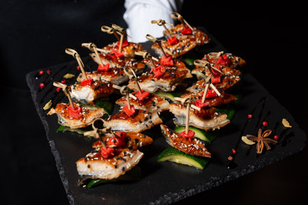 Elegant appetizer platter featuring teriyaki-glazed eel slices on zucchini, garnished with sesame seeds and red pepper accents.の写真素材