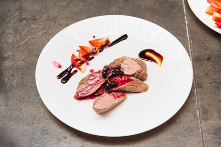 Sliced duck breast served with a dark berry reduction, balsamic glaze, and fresh strawberries on a white plate for fine dining.の写真素材