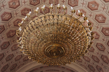Elegant golden chandelier with detailed patterns hanging below a beautifully ornate, decorated ceiling, showcasing intricate artistry and luxury. Perfect for concepts of opulence, interior design, or architectural detailing.の写真素材