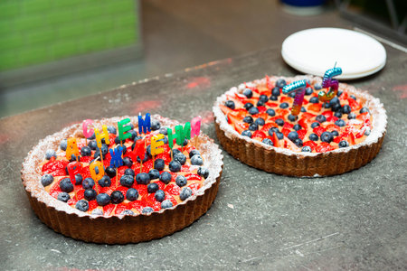 Two festive fruit tarts topped with strawberries and blueberries, decorated with birthday candles and colorful lettering.の写真素材