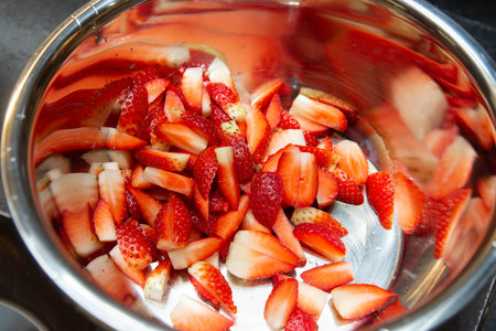 Close-up of freshly sliced strawberries in a shiny metal bowl, ready for use in dessert, salad, or garnish recipes.の写真素材