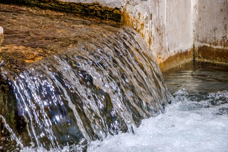 Clear water flowing over stone edge in rustic setting.