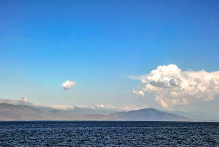 Tranquil mountainous horizon with open sea and expansive cloudy sky.