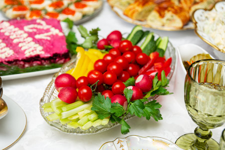 A colorful arrangement of fresh vegetables including radishes, cucumbers, tomatoes, and peppers on a glass platter, perfect for festive gatherings or healthy snack options.の写真素材