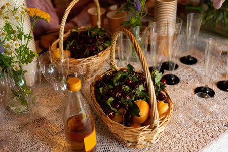 A summer picnic setup features wicker baskets filled with fresh cherries and apricots. vibrant blooms and glassware add charm to the table setting, perfect for outdoor gatherings.の写真素材
