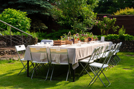 A long dining table set for an outdoor gathering, surrounded by greenery. the table is elegantly...