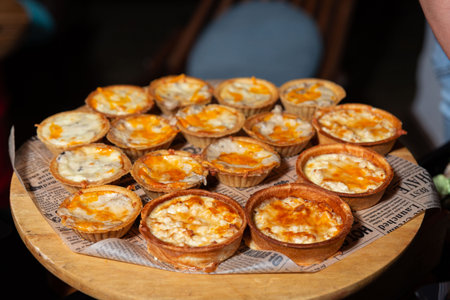 A variety of freshly baked quiches are displayed on a rustic wooden table covered with newspaper....