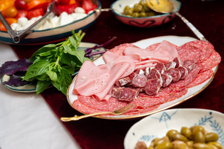 A beautifully arranged italian charcuterie platter features assorted cured meats, fresh basil, and vibrant vegetables. perfect for gatherings and gourmet occasions.の写真素材