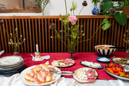 An elegantly arranged table features assorted appetizers including meats, cheeses, and vegetables. the setting includes floral decorations and fine tableware, ideal for gatherings.の写真素材