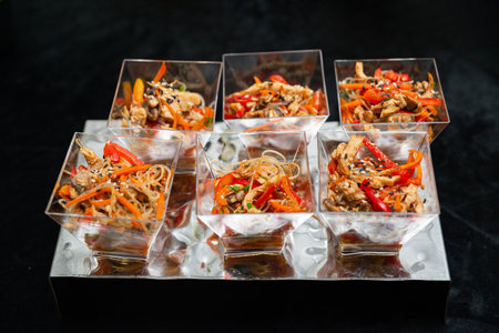 A creative arrangement of asian noodle appetizers in clear square cups. brightly colored vegetables...