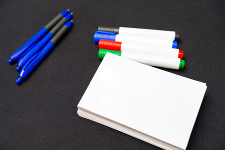 A set of blue pens and colorful markers next to a stack of blank index cards on a dark background, ideal for organization and planning activities.の写真素材