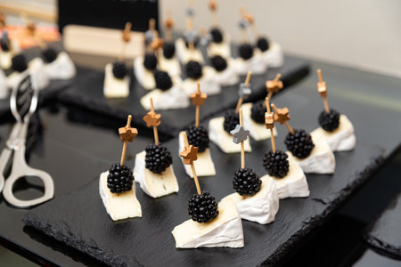 A stylish display of gourmet appetizers featuring creamy cheese topped with fresh blackberries, neatly arranged with decorative skewers, perfect for sophisticated gatherings.の写真素材