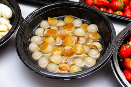 A black bowl filled with golden caramelized onions in a light syrup, surrounded by fresh strawberries.の写真素材