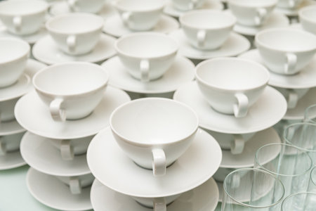 A neatly arranged collection of white porcelain tea cups and saucers. the minimalist design offers a sense of elegance, perfect for hospitality or event settings.の写真素材