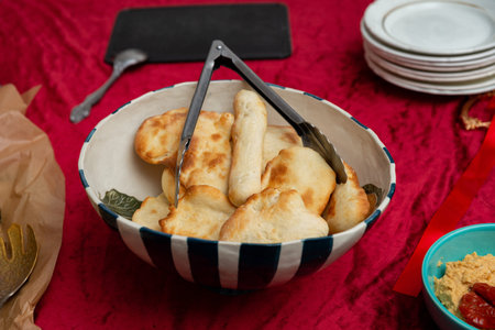 A large striped ceramic bowl filled with assorted small flatbreads and breadsticks sits on a deep...