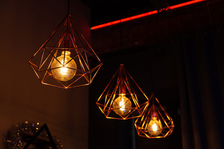 Modern hanging pendant lamps in geometric metal cages with glowing Edison bulbs, warm ambient...