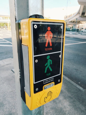 Tashkent, Uzbekistan - April 10, 2026 - Yellow push button box with red and green pedestrian icons for safe street crossing at traffic lights.