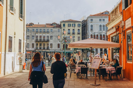 VENICE, ITALY - April 2. 2023: People are sitting at the outside terrace of a small cafe in Venice,...
