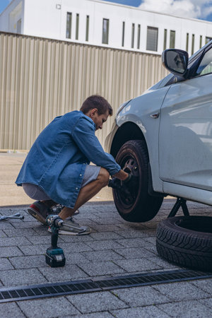 Young man in unscrewing lug nuts on car wheel in process of new tire replacement,using wrench while changing flat tire on the road.の写真素材