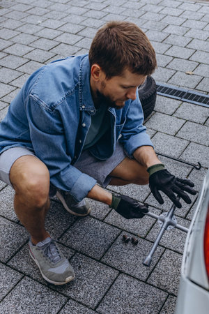 Young man in unscrewing lug nuts on car wheel in process of new tire replacement,using wrench while changing flat tire on the road.の写真素材