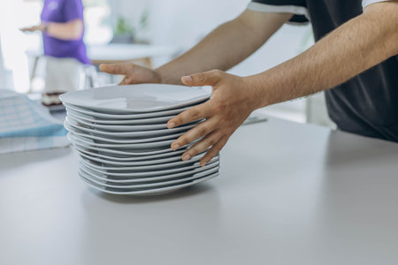 Close-up of hands holding a stack of white plates, ready to be set out for serving. High quality...