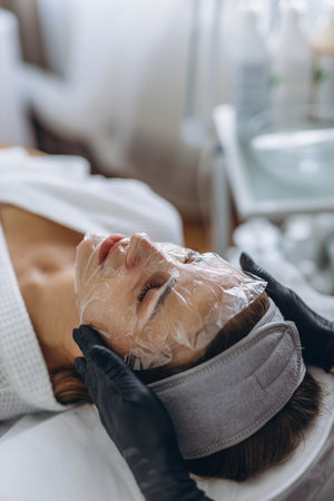 Cosmetologist cleanses young woman's face using professional skincare products. High quality photo