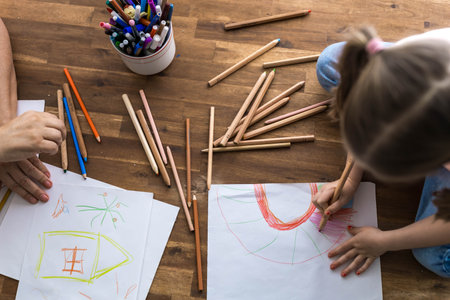 A 5-year-old girl happily draws at a table surrounded by a rainbow of colorful pencils,top view