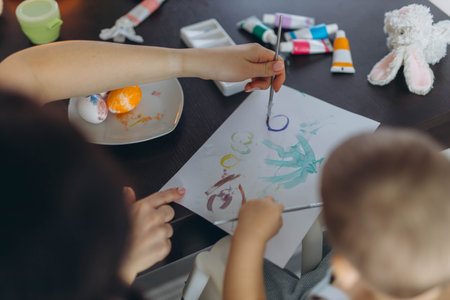 Little boy and his mother painting eggs together. Easter celebration and motherhood bonding concept
