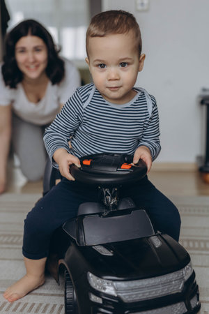 Mother and child playing in childrenroom, with the toddler sitting on a toy car, enjoying fun moment. High quality photoの写真素材