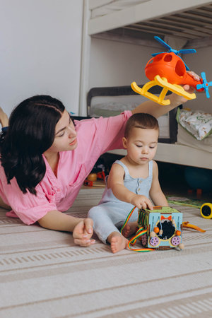 Mother and baby playing together with developmental toys, sitting on the floor, fostering learning....
