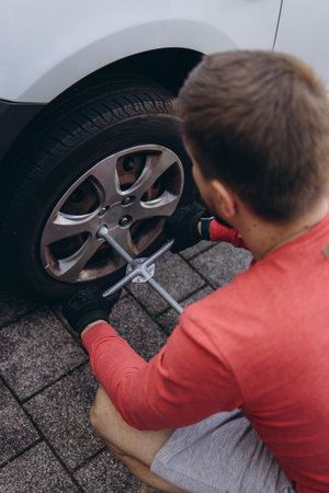 Man changing car tire on roadside using tools, vehicle lifted on jack. Concept of auto repair,...