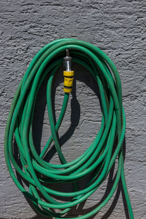 Green garden hose neatly coiled and hanging on an exterior wall, ready for outdoor watering or...