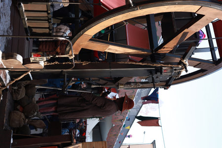 Vintage-style wooden Ferris wheel operated manually by a man in historical costume at a festive Christmas market. Family fun and tradition.の写真素材