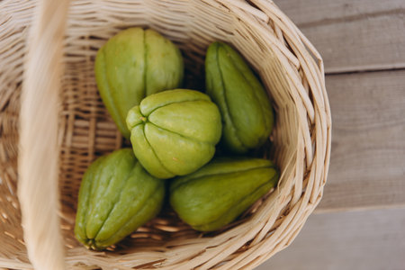 Several fresh green chayote fruits in a wicker basket top view. Organic tropical vegetable harvest....