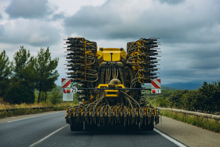 Large agricultural machine with multiple hoses and parts driving on rural road. Farming equipment transport in countryside landscape. High quality photoの写真素材