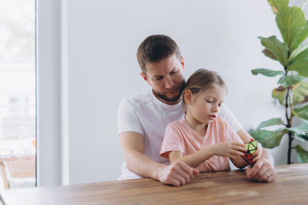 Father and daughter play with a puzzle cube at home, sitting at a wooden table and enjoying mindful time togetherの写真素材