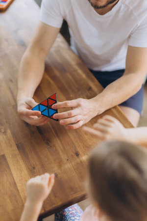 Hands of a child and adult playing together with a colorful triangular puzzle on a wooden table,...